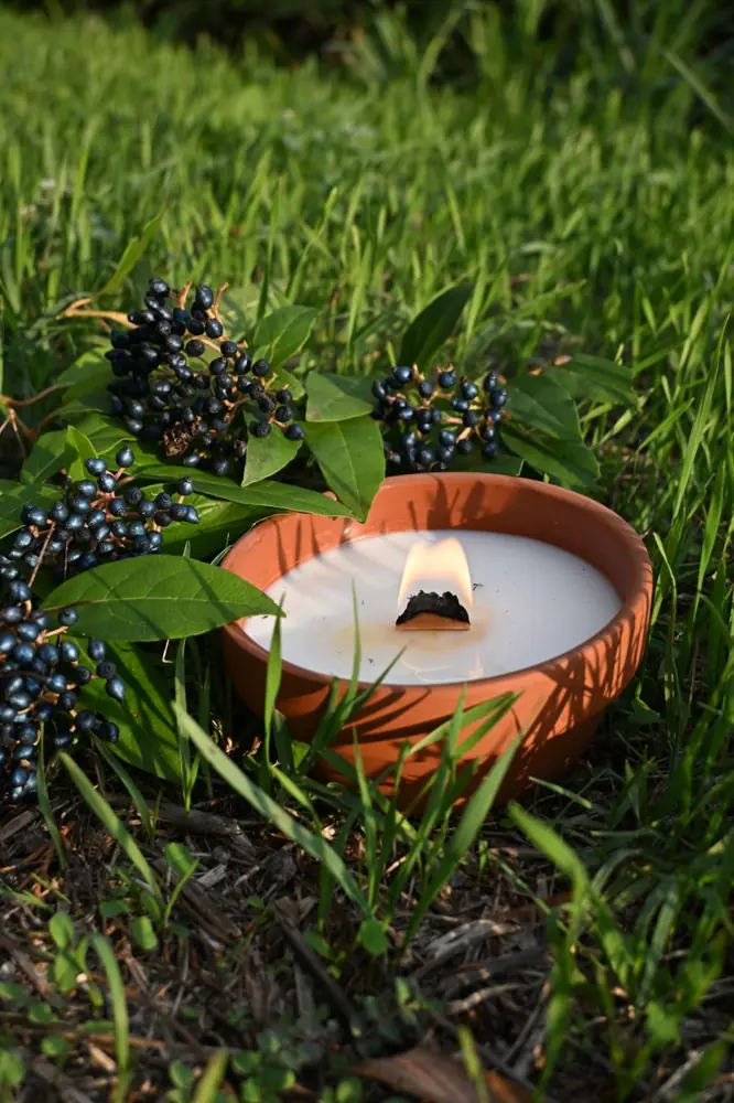 Bougie allumée dans un pot en terre cuite, dans l'herbe au soleil couchant