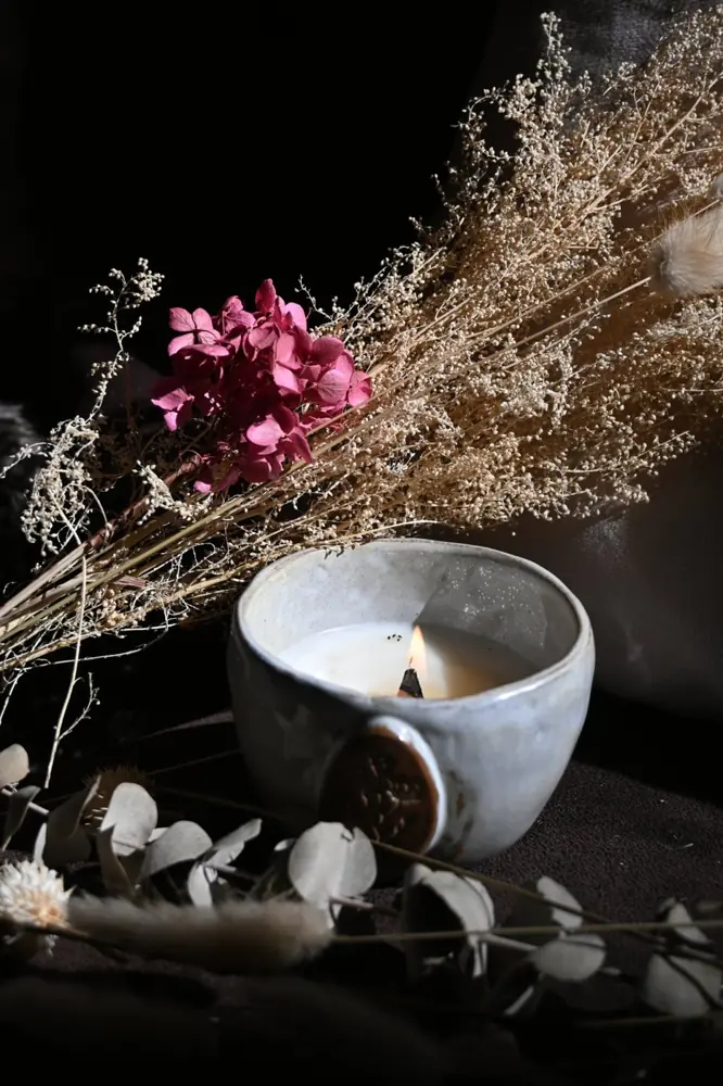 Bougie allumée dans un bol en céramique, entourée de fleurs séchées et d'eucalyptus