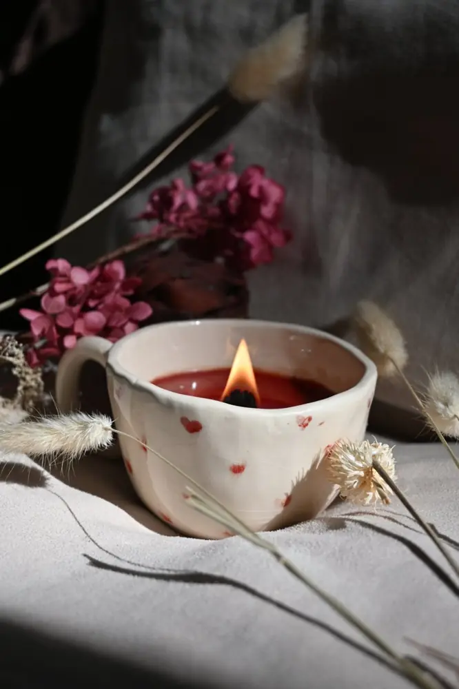 Bougie à la cire rouge dans une tasse en céramique décorée de petits cœurs rouges